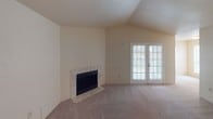 This single-floor residence offers a well-organized layout with functional living spaces throughout. The living room serves as the heart of the home, featuring vaulted ceilings that lend an open, airy feel, soft carpeted flooring, a classic tile-surround fireplace, and French doors that invite natural light and provide access to the outdoors. The galley-style kitchen is efficiently designed with white cabinetry, granite-look laminate countertops, hardwood-style flooring, a stainless steel sink, and black appliances including a refrigerator, microwave, and electric range. The bedrooms are comfortably appointed with plush carpet, ceiling fans with integrated lighting, and windows fitted with blinds for privacy and light control. One bedroom connects to a spacious walk-in closet equipped with multiple hanging rods and a built-in shelving unit, providing generous storage capacity. The bathrooms each feature a full tub-shower combination with white tile surround, chrome fixtures, and a vanity with a granite-look countertop. Throughout the home, a neutral warm beige color palette and textured ceilings create a cohesive, understated ambiance that is both practical and inviting.