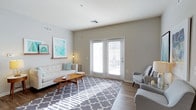 This single-floor residence offers a clean, modern aesthetic defined by neutral tones, hardwood-style flooring, and an abundance of natural light. The living area serves as the heart of the space, featuring smooth white ceilings with ample height, crisp white trim, and soft gray walls that create a calm and inviting atmosphere. A standout feature is the set of French doors that open to the outside, flooding the room with sunlight and providing a seamless connection to the outdoors. The living space is generously proportioned, offering comfortable room for both lounging and entertaining. Recessed HVAC vents are thoughtfully integrated into the ceiling, ensuring a clean and uncluttered look. The overall design sensibility is contemporary and minimalist, with a light color palette that enhances the sense of openness. The hardwood-style flooring runs throughout, adding warmth and cohesion to the interior. Whether used as a primary residence or a secondary retreat, this space balances functional living with a bright, airy ambiance that makes everyday life feel effortless and comfortable.