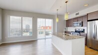 This well-appointed two-bedroom, two-bathroom residence offers a thoughtfully designed single-floor layout with modern finishes throughout. The open-concept living and kitchen area serves as the heart of the home, featuring light wood-tone flooring, pendant lighting with gold accents, and a granite-topped kitchen island with an integrated sink. The kitchen is equipped with stainless steel appliances, a classic white subway tile backsplash, and sleek dark-wood cabinetry with brushed gold hardware. Large sliding glass doors open to a private balcony, flooding the living space with natural light and framing panoramic city views.

The spacious primary bedroom is carpeted for comfort and features generous windows with urban skyline views, connecting to a well-organized walk-in closet with built-in shelving and hanging rods. The second bedroom also offers carpet flooring and a large window with city views. Both bathrooms are finished with granite-top vanities, dark wood cabinetry, white subway tile tub surrounds, and large-format white tile flooring. Two hallways connect the living areas to the bedrooms, maintaining a clean and efficient flow. Neutral gray walls and consistent light flooring throughout create a bright, cohesive, and contemporary ambiance.