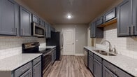 This single-story residence offers a thoughtfully designed layout with contemporary finishes throughout. The galley-style kitchen is a standout feature, showcasing slate-gray cabinetry, granite countertops, a classic white subway tile backsplash, and a full suite of stainless steel appliances including a range, microwave, refrigerator, and dishwasher. Wood-look luxury vinyl plank flooring runs throughout the main living areas, adding warmth and durability.

The living room impresses with vaulted ceilings, a ceiling fan, and rich hardwood-style flooring that extends the sense of openness. French doors flood the space with natural light and provide access to the outdoors. A chandelier-lit dining area connects seamlessly to the kitchen.

The primary bathroom features a double vanity with granite countertops and gray cabinetry, mirroring the design language of the kitchen. A secondary bathroom offers a single vanity with matching finishes and a full tub-shower combination. Bedrooms are carpeted for comfort and include ceiling fans and windows that bring in natural light. The cohesive neutral color palette and consistent use of gray cabinetry and granite surfaces give this home a modern, move-in-ready appeal.
