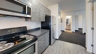 Located at 1260 Ferry St in Eugene, Oregon, this two-bedroom, two-bathroom unit offers a practical and efficiently designed single-floor layout. The kitchen is a standout feature, outfitted with stainless steel appliances including a refrigerator, electric range, built-in microwave, and dishwasher. Cabinetry in a textured gray finish pairs with dark countertops, creating a modern, cohesive aesthetic. Light vinyl flooring in the kitchen provides easy maintenance, while a window allows for natural light.

Both bedrooms are carpeted in a neutral gray tone and feature clean white walls, dark baseboards, and windows fitted with horizontal blinds that let in natural light. Each bedroom includes closet storage — one with sliding doors and another with bifold doors — providing ample organization space. A total of three closets are distributed throughout the unit.

The two full bathrooms each feature a tub/shower combo with white surround walls and chrome fixtures, maintaining a clean and functional design. The overall color palette throughout the unit is neutral and bright, with white walls and light ceilings contributing to an open, airy feel. The living area completes the layout, offering a connected flow from the kitchen through the rest of the space.
