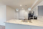 This single-floor residence offers four bedrooms and two bathrooms within a thoughtfully designed layout. The open-concept kitchen and living area serves as the heart of the unit, featuring striking marble-look countertops extending across both a peninsula with an integrated sink and a freestanding island. Spherical pendant lights hang above the peninsula, complementing recessed ceiling lighting throughout. The kitchen is equipped with stainless steel appliances, including a refrigerator, electric range, and over-the-range microwave, all set against a classic white subway tile backsplash. Gray cabinetry with sleek hardware provides ample storage.

The living area features durable wood-look flooring, while the bedrooms are finished with plush carpet. Bedrooms are bright and cleanly designed, with at least one featuring a ceiling fan and a window admitting natural light. Two closets offer dedicated storage. The bathrooms include a full tub-shower combination with chrome fixtures and built-in shelving. A dedicated laundry room houses a full-size top-loading washer and dryer with overhead wire shelving. The overall aesthetic is clean, modern, and neutral throughout.