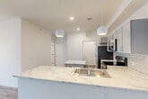 This single-floor residence offers four bedrooms and two bathrooms within a thoughtfully designed layout. The open-concept kitchen and living area serves as the heart of the unit, featuring striking marble-look countertops extending across both a peninsula with an integrated sink and a freestanding island. Spherical pendant lights hang above the peninsula, complementing recessed ceiling lighting throughout. The kitchen is equipped with stainless steel appliances, including a refrigerator, electric range, and over-the-range microwave, all set against a classic white subway tile backsplash. Gray cabinetry with sleek hardware provides ample storage.

The living area features durable wood-look flooring, while the bedrooms are finished with plush carpet. Bedrooms are bright and cleanly designed, with at least one featuring a ceiling fan and a window admitting natural light. Two closets offer dedicated storage. The bathrooms include a full tub-shower combination with chrome fixtures and built-in shelving. A dedicated laundry room houses a full-size top-loading washer and dryer with overhead wire shelving. The overall aesthetic is clean, modern, and neutral throughout.