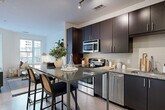 This well-designed single-floor residence offers a thoughtfully arranged layout that balances modern aesthetics with everyday functionality. The living area is bright and inviting, featuring large windows that allow natural light to fill the space, creating a warm and airy atmosphere. Neutral tones, clean white walls, and carefully curated décor contribute to a calm, contemporary ambiance throughout.

The kitchen is a standout feature, showcasing dark espresso cabinetry paired with granite countertops and a full suite of stainless steel appliances, including a range, microwave, dishwasher, and refrigerator with ice dispenser. A sleek kitchen island with bar seating provides additional prep space and a casual dining option, while light wood-style flooring and track lighting enhance the modern feel.

The bedroom is a tranquil retreat finished in soft, neutral tones with carpeted flooring, a ceiling fan, and a window that brings in natural light. A dedicated walk-in closet offers generous storage and organization.

The bathroom continues the dark cabinetry and granite countertop theme, featuring a single vanity sink, a tub-shower combination, and light tile flooring that ties the space together cohesively. Overall, this residence presents a refined, modern living experience with consistent design details throughout every room.