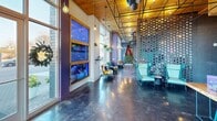 Located at 2120 N Brevard St in Charlotte, NC, this single-floor commercial space offers a striking blend of industrial and modern design elements. The open-concept layout is anchored by soaring ceilings clad in warm wood paneling, contrasted by an exposed black metal grid framework hung with Edison bulb pendant lights that cast a warm, inviting glow throughout.

Floor-to-ceiling glass windows and double glass entry doors flood the interior with abundant natural light while providing clear sightlines to the surrounding streetscape. The polished concrete floors add a sleek, durable foundation that complements the space's contemporary aesthetic.

A prominent large-format digital display screen, framed in bold yellow, serves as a focal point along one wall, ideal for community announcements or visual content. Nearby, an open latticed teal brick partition wall creates a textured visual divider, adding depth and character. A built-in wooden counter with vibrant turquoise metal stools runs along a wall featuring a striking industrial-style mural backdrop, providing a casual communal workspace or event area.

A dedicated workstation area near the windows includes a long wood desk with ample surface space. Bold, eclectic artwork and curated seating areas throughout contribute to a lively, community-oriented atmosphere, making this space well-suited for creative offices, event venues, or community-focused organizations.