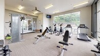 Located at 5636 Old Hickory Blvd in Nashville, TN, this fitness center offers a thoughtfully designed exercise space for residents. The room is bright and open, benefiting from floor-to-ceiling windows that flood the interior with natural light and provide views of the surrounding greenery and outdoor areas, including a pool visible from the main floor.

The exercise room is outfitted with a comprehensive selection of cardio equipment, including treadmills and elliptical machines, all positioned to take advantage of the natural light and outdoor views. A multi-station cable machine, adjustable weight bench, and a full rack of dumbbells cater to strength training needs. Wall-mounted mirrors enhance the sense of space and allow users to monitor their form during workouts.

The interior features neutral-toned carpet flooring, clean white walls, and a ceiling fan to support air circulation during workouts. A wall-mounted television provides entertainment during cardio sessions. Accent walls with a bold, dark geometric-patterned wallcovering add a modern, stylish contrast to the otherwise light and airy aesthetic. Glass entry doors connect the fitness center to adjacent amenity spaces, making it easily accessible. The overall design is functional, modern, and well-suited for a variety of fitness routines.