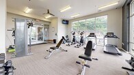 Located at 5636 Old Hickory Blvd in Nashville, TN, this fitness center offers a thoughtfully designed exercise space for residents. The room is bright and open, benefiting from floor-to-ceiling windows that flood the interior with natural light and provide views of the surrounding greenery and outdoor areas, including a pool visible from the main floor.

The exercise room is outfitted with a comprehensive selection of cardio equipment, including treadmills and elliptical machines, all positioned to take advantage of the natural light and outdoor views. A multi-station cable machine, adjustable weight bench, and a full rack of dumbbells cater to strength training needs. Wall-mounted mirrors enhance the sense of space and allow users to monitor their form during workouts.

The interior features neutral-toned carpet flooring, clean white walls, and a ceiling fan to support air circulation during workouts. A wall-mounted television provides entertainment during cardio sessions. Accent walls with a bold, dark geometric-patterned wallcovering add a modern, stylish contrast to the otherwise light and airy aesthetic. Glass entry doors connect the fitness center to adjacent amenity spaces, making it easily accessible. The overall design is functional, modern, and well-suited for a variety of fitness routines.