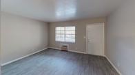 This single-floor residential unit offers a practical and comfortable layout with a variety of thoughtful finishes throughout. The main living area features durable wood-look flooring and neutral gray walls, creating a clean, open atmosphere. A ceiling fan with integrated lighting provides both comfort and illumination, while a window unit ensures year-round climate control. Natural light filters in through windows, enhancing the bright and airy feel of the space.

The kitchen is well-equipped with white shaker-style cabinetry, light stone-patterned countertops, and black appliances including a refrigerator, electric range with oven, and a built-in range hood. Light tile-style flooring and ample cabinet storage make this an efficient and functional cooking space.

The bedroom is carpeted for comfort and features a sliding glass door with vertical blinds that opens to an outdoor view, filling the room with natural light. A built-in closet with sliding mirrored doors provides generous storage.

The bathroom is neatly finished with a white vanity, stone-patterned countertop, a large mirror, and a full tub-shower combination with a curved curtain rod. Light tile flooring and clean white fixtures complete the space with a fresh, functional aesthetic.