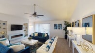 This well-appointed single-story residence offers a thoughtfully designed layout across a generous footprint. The living room is an immediate standout, featuring soaring vaulted ceilings and a ceiling fan that enhance the sense of openness and airflow. A built-in entertainment wall with integrated shelving and a sleek electric fireplace serves as the room's focal point, while a large sliding glass door with vertical blinds floods the space with natural light and provides outdoor access. Plush carpeting runs throughout the main living areas, adding warmth underfoot.

Adjacent to the living room, a dedicated dining area benefits from a bright window framed by sheer white curtains, creating an inviting atmosphere for meals. The kitchen is efficiently designed with white upper cabinetry, contrasting light blue lower cabinets, a white tile backsplash, clean countertops, a double stainless steel sink, and black appliances.

The bedroom is comfortably proportioned, featuring its own ceiling fan, plush carpeting, and ample wall space. The bathroom presents a clean, neutral aesthetic with a large framed mirror, white countertop, and updated fixtures throughout.