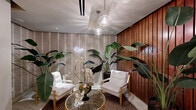Located at 215 North Pine Street in uptown Charlotte, NC, this single-floor wellness facility offers a thoughtfully curated spa experience across a comfortable footprint. The space is designed with a cohesive aesthetic that balances functionality with refined, boutique-style elegance.

The entryway and hallway feature white large-format tile flooring with contrasting inlay strips, setting a clean, polished tone carried throughout the space. Walls are adorned with a distinctive patterned wallcovering in muted, neutral tones that adds texture and sophistication. Exposed white pipes and industrial-style ceiling elements provide an urban edge that complements the refined interior.

A dedicated relaxation lounge serves as the heart of the space, featuring textured botanical wallpaper, lush tropical plants, a geometric-patterned area rug, and elegant gold-accented furnishings. A glowing neon "Relax" sign reinforces the tranquil atmosphere, making it an inviting retreat.

The steam room is fully clad in crisp white subway tile from floor to ceiling, including tiered built-in benches, with a pebble stone floor that adds a natural, grounding contrast. The locker room is well-appointed with built-in storage lockers, a gold-accented bench, curated artwork, and lush greenery. The bathroom is accessible and clearly marked, maintaining the same clean, upscale design language found throughout the entire facility.