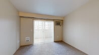 Located in Spokane Valley, WA, this single-floor, two-bedroom, two-bathroom unit offers a practical and well-organized layout. The kitchen features light wood cabinetry, a peninsula with a built-in sink and countertop workspace, a white electric range, and a refrigerator — all under a textured ceiling with overhead lighting. The open design allows for easy flow into the main living area, which is carpeted and filled with natural light from a large sliding glass door fitted with vertical blinds. The sliding door opens to an outdoor space and is complemented by a wall-mounted AC unit, providing year-round comfort. The primary bedroom is a well-proportioned carpeted space featuring the same sliding glass door access and natural light. The second bedroom offers a quieter setting with a window overlooking the exterior and soft carpet underfoot. Both bathrooms include tile flooring, light wood vanity cabinetry, and a tub-shower combination. A dedicated laundry room houses a full-size washer and dryer with an overhead shelf for added storage. A hallway and closet round out the layout, providing practical storage solutions throughout. Warm neutral tones carry consistently across all rooms, giving the unit a cohesive and understated character.