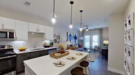This single-floor residence showcases a thoughtfully designed open-concept layout that seamlessly connects the kitchen, dining, and living areas. The kitchen is a standout feature, equipped with stainless steel appliances, two-tone cabinetry pairing white uppers with dark lowers, a subway tile backsplash, and a generous island with seating for multiple guests. Industrial-style pendant lights hang above the island, adding a modern touch.

The living area flows naturally from the kitchen and is bathed in natural light from French doors that open to an outdoor space. A ceiling fan overhead and stylish décor, including bold blue abstract artwork, give the room a welcoming yet contemporary feel. Wood-look flooring runs throughout the main living spaces.

The bedrooms are well-appointed, each featuring ceiling fans and large windows that invite natural light. One bedroom highlights a tall upholstered headboard flanked by rattan pendant lights, while another offers a wide dresser and a round mirror. The bathroom includes a tub-shower combination, a white quartz vanity, and modern gray cabinetry with ample storage. Overall, the space balances modern design with functional, comfortable living.