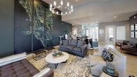 Located at 701–799 5th St in Oswego, Illinois, this single-floor community clubhouse is designed with a contemporary aesthetic that balances comfort and functionality. The open-concept main area serves as the centerpiece of the space, featuring a stylish lounge with plush seating, a round marble-top coffee table, and a dramatic large-scale abstract artwork displayed against a deep charcoal accent wall. A modern chandelier overhead adds an elegant focal point, while light hardwood flooring and abundant natural light from tall windows create a warm, inviting atmosphere throughout.

Adjacent to the lounge is a fully equipped kitchen finished with dark cabinetry, granite countertops, and stainless steel appliances including a refrigerator, oven, and microwave. A long countertop with an under-mount sink and ample workspace makes this area highly functional for gatherings and everyday use. Clerestory windows allow natural light to pour in, enhancing the open feel.

A dedicated conference and dining room offers a natural wood farmhouse-style table surrounded by mixed seating, a wall-mounted flat-screen television, and a built-in media console with decorative greenery. Large windows dressed with sheer curtains and blinds provide outdoor views and additional natural light. A separate workstation area accommodates multiple desks with task seating, making it well-suited for co-working or resident use.
