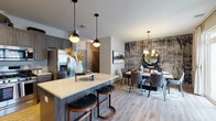 Located at 372 Wheelers Farms Rd in Milford, Connecticut, this thoughtfully designed single-floor residence offers a refined blend of modern aesthetics and functional living. Light wood-style flooring flows throughout, tying together each space with warmth and continuity. The open-concept kitchen is a standout feature, showcasing rich dark wood cabinetry that extends to the ceiling, a classic white subway tile backsplash, gleaming quartz countertops, and a full suite of stainless steel appliances including a gas range. A central island with seating provides an ideal space for casual dining or entertaining. The adjacent dining area makes a dramatic statement with a bold, textured accent wall in earthy abstract tones, complemented by a round mirror, a stylish chandelier, and direct access to natural light through large windows and a glass door. The living room is anchored by a striking blue accent wall, large windows that invite abundant natural light, and an open, inviting layout. The primary bedroom is a serene retreat featuring wood flooring, soft neutral tones, natural light from a well-positioned window, and a generous full bathroom complete with a dual-sink vanity and a glass-enclosed shower. A secondary bathroom offers a clean, tile-floored layout with a combination tub and shower. Every room in this residence reflects careful attention to detail and contemporary design sensibility.