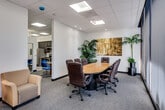 Located at 888 N Main St in Santa Ana, California, this single-floor professional office space is thoughtfully designed to accommodate a variety of business functions. The centerpiece of the suite is a well-appointed conference room featuring a large oval wood table surrounded by executive leather chairs, floor-to-ceiling windows with vertical blinds that allow ample natural light, and lush potted plants that add a touch of warmth. A bold abstract painting anchors the room's decor, creating an inviting yet professional atmosphere. Adjacent to the conference room is a comfortable waiting area furnished with soft yellow armchairs, floor lamps, and a mirrored sliding partition that visually expands the space. The suite also includes a dedicated dental operatory with blue dental chairs and professional equipment, reflecting the space's suitability for medical or clinical use. A fully equipped kitchenette offers dark cabinetry, stainless steel appliances including a refrigerator, range, and microwave, as well as marble-style countertops and wood-look flooring. The bathroom is clean and functional, featuring a walk-in glass shower, a rich wood vanity, and modern fixtures. Throughout the suite, recessed and panel lighting, neutral carpeting, and a drop ceiling create a cohesive, professional environment.