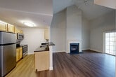This two-story, one-bedroom, one-bathroom residence at 100 Thompson Farm Rd in Bedford, Massachusetts offers a well-designed layout across two levels. The main floor features an open-concept living and kitchen area connected by a welcoming entrance and hallway. The kitchen is outfitted with light maple cabinetry, dark granite countertops, stainless steel appliances including a range, microwave, dishwasher, and refrigerator, and hardwood-style flooring that continues throughout the home. The living room is a standout space, highlighted by soaring vaulted ceilings, a classic white-mantled fireplace, and a ceiling fan, lending the area a warm and airy ambiance. A staircase leads to the upper level, which includes a loft space and a dedicated laundry room with an in-unit washer and dryer tucked under a sloped ceiling. The spacious primary bedroom features a large window with neighborhood views, ample natural light, and generous closet space. The full bathroom is clean and functional, offering a tub/shower combination, vanity with stone countertop, and hardwood-style flooring. Two closets and additional storage complete this thoughtfully arranged home in Bedford, MA.