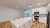 This contemporary single-floor residence is designed with clean lines and a bright, cohesive aesthetic carried throughout every room. Light wood-tone flooring runs continuously across the entire space, lending warmth and visual continuity from the entry hallway to the bedrooms.

The kitchen serves as a central highlight, featuring white flat-panel cabinetry extending to the ceiling, a classic gray tile backsplash, and a full suite of stainless steel appliances including a range, microwave, dishwasher, and refrigerator. A generously sized center island topped with white quartz provides ample prep and gathering space, illuminated by a pair of polished pendant lights. Natural light filters in through multiple windows, brightening the open kitchen and adjacent areas.

A well-proportioned hallway with louvered closet doors connects the sleeping quarters. The bedrooms are clean and versatile, each equipped with ceiling fans and ample space for varied layouts. The primary bathroom impresses with a dual-sink vanity topped in white quartz, a large wall mirror, stylish sconce lighting, a tiled walk-in shower, and access to a walk-in closet. The secondary bathroom offers a full soaking tub with square white tile surround, a single vanity, and a mirror. Recessed lighting throughout enhances the overall bright, modern ambiance of this well-designed residence.