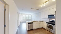 Located at 200 Hudson Ct in Wheeling, IL, this well-appointed one-bedroom, one-bathroom residence offers a thoughtfully designed layout across a single floor. The open-concept kitchen and living area serves as the heart of the unit, featuring crisp white shaker cabinetry, light granite countertops, a peninsula with an undermount sink, and a full suite of stainless steel appliances including a gas range, microwave, and dishwasher. Pendant lights suspended from a track rail add a modern touch overhead, while hardwood-style flooring runs throughout the main living space. A large trio of windows floods the living area with natural light and provides views of the surrounding greenery, complemented by a private entry door for added convenience. The carpeted bedroom is a comfortable retreat, offering its own window with outdoor views and direct access to a hallway leading to the full bathroom, which includes a vanity with ample storage. A dedicated closet and additional hallway storage provide practical organization throughout. The clean, neutral palette and modern finishes create a cohesive, move-in-ready ambiance suited for comfortable everyday living.