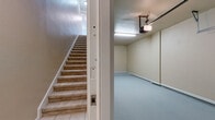 This two-floor residence offers a thoughtfully designed layout with a blend of practical and comfortable living spaces. The attached garage provides direct interior access via a carpeted staircase, featuring a smooth epoxy-coated floor, a motorized garage door opener, and ample clearance for vehicle storage.

The main living level showcases warm hardwood flooring and elegant crown molding throughout. The kitchen is equipped with white cabinetry, black appliances including a refrigerator, range, and built-in microwave, and a peninsula with a light stone countertop and stainless steel sink. This peninsula opens directly to the living and dining area, which features plush neutral carpeting and seamless flow between spaces.

The bedrooms are carpeted and finished with crown molding, offering a calm and comfortable atmosphere. The primary bedroom is generously sized with multiple windows that invite natural light and include a ceiling fan for added comfort. Additional bedrooms are well-proportioned with six-panel doors and clean neutral walls.

The bathroom features a white vanity with stone countertop, an undermount sink, polished chrome fixtures, a large framed mirror with vanity lighting above, and hardwood flooring. Throughout the home, warm beige tones, white trim, and consistent finishes create a cohesive and inviting ambiance.
