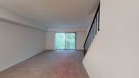 Located at 1800 Laurel Rd in Lindenwold, NJ, this two-story residence offers a well-organized layout spread across two levels connected by a staircase with a sleek black metal railing. The main level features a kitchen equipped with rich dark wood cabinetry, granite-style countertops, stainless steel appliances including a dishwasher and range, and wood-look flooring that adds warmth to the space. A pass-through window connects the kitchen to the adjacent living area, enhancing the open feel. The living room is generously sized with plush carpeting and a large sliding glass door fitted with vertical blinds, opening to a view of lush greenery that brings natural light into the space. A staircase from the main level leads to the upper floor, where the bedrooms are situated. The bedrooms are carpeted and well-lit by large windows with outdoor views, and include closet space with louvered doors. The bathroom features light wood-look flooring, a white vanity with ample cabinet storage, and a shower-tub combination. Throughout the home, neutral tones and clean finishes create a bright, move-in ready environment suitable for comfortable everyday living.