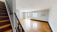 Located at 38 1/2 Wolden Rd in Ossining, NY, this two-bedroom, two-bathroom residence spans two floors with a well-planned layout that maximizes both function and comfort. The upper main level hosts the spacious living and dining areas, adorned with warm, polished hardwood floors and light gray walls that create a bright, neutral atmosphere. Sliding glass doors and windows flood the living room with natural light while opening to a balcony overlooking lush, mature trees and a landscaped yard. The kitchen features white shaker cabinetry, gray quartz countertops, a subway tile backsplash, and stainless steel appliances, offering a clean, modern aesthetic. The generously sized primary bedroom provides ample space and includes a wall-mounted AC unit and natural light from a double-pane window. A loft adds versatile bonus space, while six closets throughout ensure abundant storage. The bathroom is finished with large-format floor tiles, white subway wall tiles accented by a mosaic border, and a soaking tub. A dedicated laundry area and hallway round out the practical amenities. A decorative iron staircase railing adds an elegant architectural touch, complementing the home's overall clean and inviting character.
