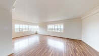 This single-floor unit is defined by its clean, open layout and consistent use of rich hardwood flooring throughout the main living areas. Large windows are a defining architectural feature, appearing in multiple rooms and framing sweeping views of the surrounding cityscape and lush treetops. The generous living and dining areas benefit greatly from this window placement, with natural light reflecting off the polished floors and brightening the crisp white walls. Crown molding adds a refined detail to the living space, lending a classic touch to the otherwise contemporary interior.

The kitchen is designed for functionality, featuring white flat-front cabinetry extending to the ceiling for ample storage, sleek light-toned countertops, a stainless steel sink, and modern stainless steel appliances including an electric range. Light tile flooring completes the clean, well-organized layout.

The bedroom is notably spacious, offering built-in closet storage with mirrored doors and open shelving, alongside direct access to the bathroom. The bathroom presents a white vanity with a mirror, a glass-enclosed shower stall, and light tile floors, maintaining the unit's consistent bright and neutral aesthetic throughout.