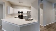 Located at 2900 Sunridge Dr in Austin, TX, this single-story unit offers a thoughtfully designed open-concept layout that seamlessly connects the living, dining, and kitchen areas. The living room is highlighted by vaulted ceilings and a front entryway with a full-lite door flanked by windows, allowing natural light to fill the space. Rich, dark hardwood-style flooring flows throughout the main living areas, creating a warm and cohesive aesthetic.

The kitchen is a standout feature, boasting white shaker-style upper cabinets, gray lower cabinets, crisp white quartz countertops, and a peninsula with an undermount sink. A full suite of stainless steel appliances — including a range, microwave, dishwasher, and refrigerator — completes the modern look.

The bedrooms feature lighter hardwood-style flooring, ceiling fans, and ample natural light from well-sized windows with blinds. The bathrooms are finished with gray vanity cabinetry, white quartz countertops, framed mirrors, and hardwood-style flooring. One bathroom includes a soaking tub with shower, while another offers a vanity with toilet. Neutral gray-toned walls throughout the unit provide a clean, versatile backdrop suited to a variety of interior styles.