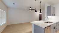 Located in Kingwood, this single-story home offers a clean, contemporary design across three bedrooms and two bathrooms. The layout flows efficiently, with light wood-toned flooring extending throughout the space, creating a cohesive and airy feel.

The kitchen serves as a functional centerpiece, featuring gray shaker-style cabinetry, stainless steel appliances including a French door refrigerator and built-in microwave, and a white quartz peninsula with an undermount sink. Striking black pendant lights hang above the peninsula, adding a modern contrast. A built-in wine rack above the upper cabinets provides additional storage and character. Natural light enters through multiple windows fitted with white blinds.

The bedrooms are well-proportioned and bright, each equipped with a sleek black ceiling fan and windows that invite natural light. Raised-panel doors in a dark finish add a refined touch throughout.

Both bathrooms maintain the home's modern aesthetic, with gray vanity cabinetry, white quartz countertops, black hardware accents, and light flooring. One bathroom features a glass-enclosed shower-tub combination with gold-toned framing. The overall ambiance is clean, contemporary, and move-in ready.