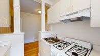 Located at 21 Wendell St in the heart of Cambridge, MA, this single-floor residence blends classic New England charm with practical design. Warm hardwood floors run throughout the space, lending a sense of continuity and brightness to every room.

The living area is open and airy, with neutral walls and clean white trim that create a welcoming ambiance. Natural light filters in through well-placed windows, adding warmth to the hardwood floors beneath.

The bedrooms are comfortably sized, with the same gleaming hardwood flooring and crisp white walls. One bedroom features a dedicated closet with a built-in rod for storage, along with a window that offers a pleasant neighborhood view. The rooms are connected by white-paneled doors that add a touch of traditional character.

The kitchen is compact yet efficiently arranged, featuring white cabinetry, a gas range, an under-cabinet range hood, and a stainless steel sink. A distinctive decorative column detail adds architectural interest, framing the transition between the kitchen and the adjoining hallway.

The bathroom is a standout, showcasing a classic black-and-white aesthetic with a multi-colored checkered tile floor, black accent tile trim, a soaking tub, a vanity with mirror, and a cast-iron radiator. A window brings in natural light, completing the vintage-inspired design.