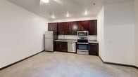This two-floor apartment in Burlington, NC offers a well-designed layout spread across two equally sized levels. The kitchen is a standout feature, equipped with rich dark-wood cabinetry, granite countertops, stainless steel appliances including a refrigerator, dishwasher, microwave, and range, plus a built-in wine rack. Recessed lighting illuminates the open living area, which features polished concrete flooring. Two bathrooms serve the unit — one on each floor — both finished with matching granite vanity tops and dark wood cabinetry. The upper level bathroom includes warm hardwood flooring, while the lower level offers tile. Clean white walls and consistent finishes throughout give the space a modern, cohesive aesthetic.