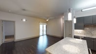 This contemporary single-floor Dallas residence showcases a thoughtfully designed open-concept layout that seamlessly connects the kitchen and living areas. Rich, dark hardwood flooring flows throughout the main living space, adding warmth and sophistication to the modern aesthetic. The kitchen features striking granite countertops with subtle veining, complemented by sleek pendant lighting that adds an elegant finishing touch. The open living area is bathed in natural light streaming through a glass sliding door that leads to a private balcony, offering a connection to the outdoors. A ceiling fan centered in the living space ensures year-round comfort. Recessed lighting and stylish pendant fixtures illuminate the space with a clean, contemporary feel. Neutral white walls provide a versatile backdrop throughout, while gray interior doors add a modern, coordinated design element. The layout is both functional and inviting, offering a generous sense of openness. Every detail of this Dallas residence reflects a commitment to modern finishes and thoughtful design, making it a refined and comfortable urban living space.