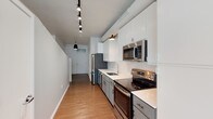 Located at 4545 Forest Park Ave in St. Louis's vibrant Forest Park Southeast neighborhood, this loft-style unit offers an open, single-floor layout with a distinctly industrial character. Exposed ductwork, whitewashed concrete ceilings, and track lighting define the aesthetic throughout, creating a spacious, urban atmosphere that balances raw architectural detail with contemporary updates.

The open living area is generously proportioned, featuring warm hardwood flooring, a ceiling fan, and a large multi-pane window that floods the space with natural light and frames views of the surrounding cityscape. Track lighting runs the length of the unit, complementing pendant fixtures that add warmth to the industrial framework.

The galley-style kitchen is well-equipped with stainless steel appliances, including a refrigerator, range, microwave, and dishwasher. White upper cabinetry contrasts with gray lower cabinets beneath clean white countertops, while a classic subway tile backsplash adds timeless detail. A stainless steel double sink anchors the workspace.

A central half-wall divides the living and kitchen zones, enhancing the open feel while providing subtle spatial definition. The bathroom features a glass-enclosed walk-in shower with full subway tile surround and chrome fixtures. An electrical panel is conveniently accessible near the entryway.