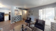 This single-level unit offers a thoughtfully designed layout that maximizes functionality across its one-bedroom, one-bathroom floor plan. The living area serves as the heart of the space, featuring dark hardwood-style flooring, a white brick fireplace as a focal point, and a sliding glass door that introduces natural light and provides outdoor access. Cool gray walls create a cohesive, modern palette throughout.

The kitchen is well-equipped with white cabinetry, granite-style countertops, a gray tile backsplash, and black appliances including a refrigerator and electric range alongside a stainless steel microwave. A pass-through bar area connects the kitchen to the living space and includes a built-in wine rack, adding a practical and stylish touch.

The bedroom is carpeted for comfort and includes a ceiling fan with light fixture, neutral gray walls, and direct access to a walk-in closet. The full bathroom features a granite-topped vanity, a large mirror, and a tub-shower combination with classic white tile surround. A textured ceiling is consistent throughout the unit, complementing the overall design aesthetic.
