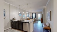 This thoughtfully designed single-story residence offers 2 bedrooms and 2 bathrooms across a comfortable and functional floor plan. The open-concept kitchen and living area serves as the heart of the home, featuring dark cabinetry contrasted by light granite countertops, stainless steel appliances, and a kitchen island with a double sink. Three pendant lights hang above the island, adding both style and practicality. The living room flows seamlessly from the kitchen and is filled with natural light from large windows and a glass-paneled door, complemented by crown molding and wood-style flooring throughout. A separate dining room with a chandelier and double-door closet provides a dedicated space for formal meals. The primary bedroom offers comfortable proportions with plush carpet flooring and a ceiling fan, while the second bedroom includes a double-door closet and easy access to a full bathroom. Both bathrooms feature granite-topped dark vanities and tile flooring. Crown molding is present throughout the main living areas, adding a refined architectural touch. The unit also includes a dedicated laundry room and three closets, ensuring ample storage throughout.