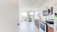 Located at 1405 Rivard St in Detroit, MI, this efficiently designed single-floor studio offers a thoughtfully organized open-concept layout that seamlessly integrates the living, dining, and kitchen areas into one cohesive space. The kitchen is a standout feature, showcasing warm wood lower cabinetry paired with crisp white upper cabinets, stone-look countertops, a matte black gooseneck faucet, and a full suite of stainless steel appliances including a dishwasher, electric range, refrigerator, and built-in microwave. Light-toned flooring runs throughout, contributing to a clean, modern aesthetic. Large windows flood the open living and dining area with natural light and offer views of the surrounding Detroit cityscape, with a bar-height table and stools making excellent use of the space near the windows. The bathroom is finished with contemporary fixtures, featuring a tub and shower combination enclosed by sleek sliding glass doors with matte black framing, complemented by matching wood vanity cabinetry. Additional conveniences include a dedicated laundry area, two closets for ample storage, and a defined entrance. The overall ambiance is bright, minimal, and modern, ideal for urban living.