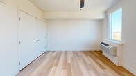 Located at 9749 SW Barber St in Wilsonville, Oregon, this efficiently designed studio offers a thoughtful layout that maximizes every square foot. Light wood-tone flooring runs throughout the entire unit, creating a warm and cohesive aesthetic. The open-concept kitchen and living area serves as the heart of the space, featuring a well-appointed kitchen with two-tone cabinetry in grey and dark wood finishes, white countertops, open shelving, and a full suite of black appliances including a refrigerator, electric range, microwave, and dishwasher. Recessed lighting illuminates the kitchen, while a French door leads directly to a private balcony overlooking a pleasant outdoor view — filling the living area with natural light. The bedroom area is clean and understated, with crisp white walls, a closet, and a wall-mounted heating unit. The bathroom is modern and stylish, showcasing a warm wood-grain vanity with white countertop, an illuminated LED-backlit mirror, and light hardwood-style flooring. Additional storage is provided through multiple closets throughout the unit. The overall ambiance is clean, contemporary, and move-in ready.