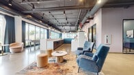 Located at 4757 Hiawatha Ave in Minneapolis, MN, this single-floor commercial space offers a thoughtfully designed, open-plan layout that blends industrial and contemporary aesthetics. The expansive floor plan is unified by polished concrete floors that reflect natural light throughout, creating a bright and airy atmosphere.

The architectural character is defined by exposed ductwork and ceiling infrastructure painted in dark tones, providing an industrial contrast to the clean white walls accented with teal and blush hues. Large floor-to-ceiling windows span multiple walls, flooding the interior with abundant natural light and offering views of the surrounding streetscape and greenery.

The space is organized into distinct functional zones. A central lounge area features plush blue velvet armchairs, modular sofas, and a marble-topped coffee table set atop a vibrant area rug. Nearby, a casual dining and collaboration zone is furnished with round tables and coordinating blue upholstered chairs with gold accents. A built-in kitchenette with dark cabinetry runs along one wall, providing functional utility.

A glass-walled private room with bold geometric wall art offers an enclosed meeting or focus area. A fireplace anchors one lounge corner, adding warmth and sophistication. Track lighting and pendant fixtures complement the natural light, ensuring the space is well-lit throughout. Curated artwork and lush plants complete the refined, welcoming ambiance.