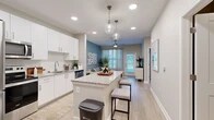 Located at 1880 SW 43rd St in Gainesville, FL, this well-appointed 2-bedroom, 2-bathroom residence offers a thoughtfully designed single-floor layout. The open-concept kitchen and living area serve as the heart of the home, featuring crisp white shaker cabinetry, granite countertops with a subway tile backsplash, and a full suite of stainless steel appliances. A central island with pendant globe lighting doubles as a breakfast bar, flowing naturally into the bright living room. The living area is accented by a calming blue feature wall, large windows with sheer drapery, and light wood-style flooring that carries throughout the main spaces. The primary bedroom is a comfortable retreat with plush carpet, dual windows, a ceiling fan, and direct access to a private en-suite bathroom. The en-suite features a granite vanity with white cabinetry and a glass-enclosed walk-in shower. The second bedroom is equally well-sized with carpet flooring and a ceiling fan. The second bathroom mirrors the same refined finishes, including a granite-topped vanity and wood-look tile flooring. A dedicated laundry room with a full-size washer and dryer and a water heater adds everyday convenience. The overall aesthetic is clean, modern, and cohesive throughout.