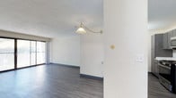 This single-floor, 1-bedroom, 1-bathroom residence offers a straightforward and functional layout designed for comfortable everyday living. The main living area is finished with smooth, dark hardwood-style flooring that provides a clean and contemporary feel throughout the space. Textured white walls add subtle character and depth, complementing the bright, neutral color palette of the interior. A notable decorative touch is the brass-accented pendant light that hangs from the ceiling, adding a warm, classic element to the living area. A sliding glass door along one wall allows natural light to filter into the space, creating an open and airy ambiance while providing access to the exterior. The ceiling features a lightly textured finish consistent with the overall style of the unit. The bedroom and bathroom, though compact, are designed to maximize utility within the footprint of the home. Overall, the residence presents a clean, move-in ready environment with simple, timeless design choices that offer a neutral backdrop easily personalized to individual tastes.