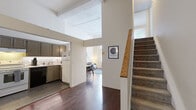 This two-story Philadelphia residence offers a well-designed layout across two floors, combining thoughtful functionality with notable architectural character. The main floor features rich, dark hardwood flooring throughout, a welcoming entryway with a staircase accented by a warm wood handrail, and an open flow between the kitchen, dining, and living areas. The kitchen is well-appointed with taupe cabinetry, white subway tile backsplash, slate tile flooring, and full appliances including a dishwasher and range. The living room is a standout space, boasting impressively tall ceilings and oversized windows that flood the room with natural light and offer urban views. A separate dining area connects seamlessly to the living space, enhancing the open feel of the main floor. Upstairs, two bedrooms continue the hardwood flooring and feature white-paneled ceilings, natural light from street-facing windows, and closet access. The primary bedroom is a comfortable retreat with warm ambient lighting, while the second bedroom offers a clean, minimalist design. Both bathrooms are finished in white tile and include full tub-shower combinations with chrome fixtures. Throughout the home, the neutral color palette, high ceilings on the main level, and consistent hardwood flooring create a cohesive and inviting atmosphere.