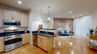 This single-floor residence offers a thoughtfully designed open-concept layout that seamlessly connects the kitchen, dining, and living areas. The kitchen is a standout feature, anchored by a curved island with a dark granite countertop, an undermount sink, and pendant lighting overhead. Light maple cabinetry lines the walls and pairs elegantly with the dark stone surfaces, while stainless steel appliances — including a gas range, microwave, refrigerator, and dishwasher — complete the space. Rich hardwood flooring flows throughout the main living areas, enhancing the warm and inviting atmosphere.

The living room is defined by a warm earth-toned accent wall, recessed lighting, and vertical blinds that allow for natural light control. A cozy nook adjacent to the kitchen provides additional flexible seating space.

The bedroom is a restful retreat featuring plush carpeting, a bold teal accent wall, and a window with outdoor views, allowing natural light to fill the room.

The bathroom is clean and functional, featuring large-format tile flooring, a white vanity with a dark stone countertop, an oval mirror, and a full tub-shower combination. Together, these spaces create a cohesive, modern living environment with consistent and stylish design details throughout.