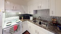 This single-floor, 2-bedroom, 1-bathroom residence offers a well-organized layout that maximizes its footprint with practical, comfortable living spaces. Warm-toned hardwood floors run throughout the home, lending a consistent and inviting character to every room.

The living area is bright and open, with a ceiling fan overhead and a window that allows natural light to fill the space. It connects directly to the kitchen, creating an easy flow between entertaining and cooking areas. The kitchen is thoughtfully appointed with white cabinetry, dark countertops, a stainless steel double-basin sink, and a standout embossed metallic tile backsplash that adds visual interest and a touch of character.

Both bedrooms are comfortably sized, each featuring hardwood floors, ceiling fans with light fixtures, and windows fitted with blinds that offer natural light and privacy. One bedroom includes a louvered closet door, adding functional storage.

The bathroom is efficiently laid out with a vanity counter, a large mirror, and a separate water closet area housing the toilet and a tub-shower combination. Clean white walls and dark hardwood floors give the bathroom a crisp, functional finish. Overall, the home presents a clean, straightforward aesthetic with consistent finishes throughout.