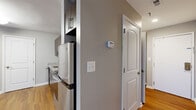 Located at 9890 Washingtonian Blvd in Gaithersburg, MD, this efficiently designed single-floor unit offers a thoughtfully arranged layout comprising a living room, kitchen, bathroom, and hallway. Warm hardwood-style flooring runs throughout the space, lending a cohesive and inviting feel to every room.

The open living area is bright and clean, featuring neutral gray walls, white trim, and a window fitted with blinds that allows natural light to fill the room. The space offers a versatile, open canvas well-suited for a variety of furniture arrangements.

The kitchen is a standout feature, equipped with rich dark-wood cabinetry, granite countertops, a stainless steel undermount sink, and a full suite of stainless steel appliances including a refrigerator, electric range, over-the-range microwave, and dishwasher. The kitchen connects smoothly to the hallway, which provides access to the rest of the unit.

The bathroom is well-appointed with a tub-shower combination featuring tile surround, dark wood cabinetry with ample storage, a white countertop vanity, and a mirrored medicine cabinet — all finished with clean, modern hardware in a brushed chrome finish.

The hallway connects the rooms efficiently, with gray walls and consistent flooring tying the overall design together. This unit delivers a modern, functional aesthetic in a compact and well-utilized footprint.