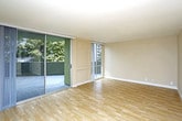 This single-floor residence is designed with a clean, functional layout that maximizes natural light and open space. The main living area is expansive, featuring warm light wood flooring and floor-to-ceiling sliding glass doors that open onto a private balcony, offering views of surrounding greenery. A second set of sliding glass doors reinforces the connection between the interior and outdoor areas, bathing the space in abundant natural light.

The kitchen is positioned at one end of the living area and features a raised peninsula counter that separates it from the main floor. Dark cabinetry contrasts with light countertops, and stainless steel appliances—including a refrigerator and microwave—are integrated into the design. Open wall shelving adds additional storage and display space beside the kitchen.

The bedrooms are carpeted for comfort and each includes large sliding windows with outdoor views. One bedroom features a mirrored sliding closet, maximizing the sense of space. The neutral, warm-toned walls throughout create a cohesive and calming ambiance.

The bathroom includes a full soaking tub with a shower combination, fitted with brushed nickel fixtures against clean white surrounds, maintaining the space's consistent understated aesthetic.