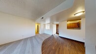 This single-floor residential unit offers a functional and comfortable layout designed for everyday living. The open main living area features a seamless transition between plush carpeting and rich hardwood-style flooring, creating a clear visual distinction between the lounge and dining zones. A textured popcorn ceiling runs throughout, and a structural beam detail adds architectural character to the living space. Natural light filters in through a window, brightening the neutral white walls.

The kitchen is efficiently arranged in a galley style, showcasing warm honey-toned wood cabinetry paired with light countertops and stainless steel appliances, including a range with over-the-range microwave, refrigerator, and dishwasher. The hardwood-style flooring continues throughout the kitchen, tying it cohesively to the main living area.

The bedrooms are carpeted for comfort and feature warm accent walls in a neutral taupe tone. Each bedroom is generously sized with ample closet storage, including built-in shelving for organization. Natural light enters through vertical blinds, lending a soft, airy feel to the private spaces.

The bathroom features a wood-vanity with a white countertop, a framed mirror with overhead lighting, and a separate water closet. The hardwood-style flooring in the vanity area adds warmth and continuity throughout the home.