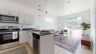 This single-floor residence offers a thoughtfully designed open-concept layout that seamlessly connects the kitchen and living area, creating a bright and cohesive living environment. The kitchen is a standout feature, boasting crisp white cabinetry with brushed nickel hardware, dark granite countertops, and a central island with pendant lighting overhead. Stainless steel appliances, including a refrigerator, range, microwave, and dishwasher, complete the functional and stylish space. Light wood-style flooring runs throughout the main living area, enhancing the clean, modern aesthetic. The living room is bathed in natural light, thanks to a large sliding glass door that opens to a private balcony, offering outdoor views and a seamless indoor-outdoor connection. A secondary window further brightens the space. The bedroom is a serene retreat with plush carpeting, a generous window with blinds, and clean white walls that create a calm, restful atmosphere. The full bathroom features dark granite countertops, white cabinetry, wood-style flooring, and a tub-shower combination. Throughout the unit, the consistent use of white walls, natural textures, and modern finishes lends a cohesive, contemporary feel.