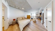 Located at 307 SW Fifth St in Fort Lauderdale, FL, this thoughtfully designed one-bedroom, one-bathroom residence combines industrial character with contemporary finishes. The open-concept living area seamlessly integrates the kitchen, dining, and living spaces, all unified by warm light wood flooring and striking exposed concrete ceilings that lend an urban loft aesthetic throughout.

The kitchen is outfitted with sleek slate-blue cabinetry, stainless steel appliances, and a built-in breakfast bar — offering both functionality and style. The living and dining area flows naturally toward floor-to-ceiling windows and a private balcony, flooding the space with natural light and framing sweeping views of the Fort Lauderdale skyline.

A natural wood room divider thoughtfully separates the bedroom from the living area, creating a sense of privacy while preserving the open feel of the space. The bedroom includes access to a dedicated walk-in closet with built-in shelving. Additional closet and utility spaces provide practical storage throughout.

The bathroom features large-format stone-look wall tiles, a glass-enclosed walk-in shower with mosaic tile flooring, and a backlit vanity mirror, delivering a clean, spa-inspired finish. A laundry area and hallway complete the well-organized floor plan of this refined urban residence.