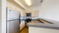 Located at 2907 N High St in Columbus, Ohio's Clintonville neighborhood, this two-floor unit offers a well-designed layout with practical finishes throughout. The kitchen is a standout feature, equipped with stainless steel appliances including a refrigerator, electric range, and over-the-range microwave. Light maple cabinetry provides ample storage, while dark laminate countertops and a peninsula with extended counter space add both style and functionality to the cooking area. The living spaces benefit from generous natural light, most notably through a large multi-pane window that frames outdoor views of the surrounding greenery and neighborhood streetscape. The soaring ceiling height in this area enhances the sense of openness and airiness. The bathroom is clean and straightforward, featuring a full soaking tub and shower combination with chrome fixtures. A dedicated utility room houses the water heater and HVAC system, keeping mechanical components neatly contained. Neutral wall tones, consistent light-colored flooring, and clean architectural lines give the unit a cohesive and understated aesthetic throughout both floors, making it a functional and comfortable space in a well-connected Columbus location.