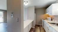 Located at 908 Ridge Square in Elk Grove Village, Illinois, this single-floor unit offers a well-organized layout designed for comfortable everyday living. Rich, wood-look plank flooring runs throughout the space, providing a warm and cohesive aesthetic from room to room.

The kitchen is outfitted with white cabinetry, a white appliance suite including a refrigerator and electric range, and a raised breakfast bar countertop that opens toward the main living area. This pass-through design creates a connected, open feel between the kitchen and living space. Ceiling-mounted lighting fixtures illuminate both areas effectively.

The living area is generously proportioned, benefiting from a large window with vertical blinds that allows natural light to filter in. A standout architectural detail is the frosted glass sliding barn door, which adds a modern, space-saving touch to the interior design.

The hallway leads to a bathroom featuring a white vanity with an integrated sink, a framed medicine cabinet mirror, and clean, neutral finishes. Adjacent to the hallway is a spacious closet area, providing practical storage solutions. The neutral gray and taupe wall tones throughout the unit create a calm, versatile backdrop suited to a variety of furnishing styles.