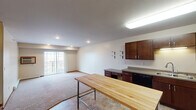 Located at 3450 38th Ave S in Fargo, North Dakota, this single-floor unit offers a practical and comfortable layout designed for everyday living. The open-concept kitchen and living area form the heart of the space, with the kitchen showcasing rich dark-wood cabinetry, ample counter space, a double-basin sink, and a full suite of black Whirlpool appliances including a refrigerator, range, over-the-range microwave, and dishwasher. Tile flooring runs throughout the kitchen and transitions to soft carpeting in the living area, which benefits from recessed lighting and access to a private balcony through a sliding glass door, bringing in natural light and outdoor views. A built-in desk and additional cabinetry provide convenient workspace within the main living area. The bedroom is generously sized with plush carpeting, a window overlooking the surrounding landscape, and baseboard heating. The full bathroom features a dark-wood vanity with a wide countertop, a large mirror with overhead lighting, and a tub-shower combination. A dedicated laundry room houses a full-size Whirlpool washer and dryer alongside a wire storage shelf. The unit also includes a wall-mounted air conditioning unit, ensuring year-round comfort throughout.